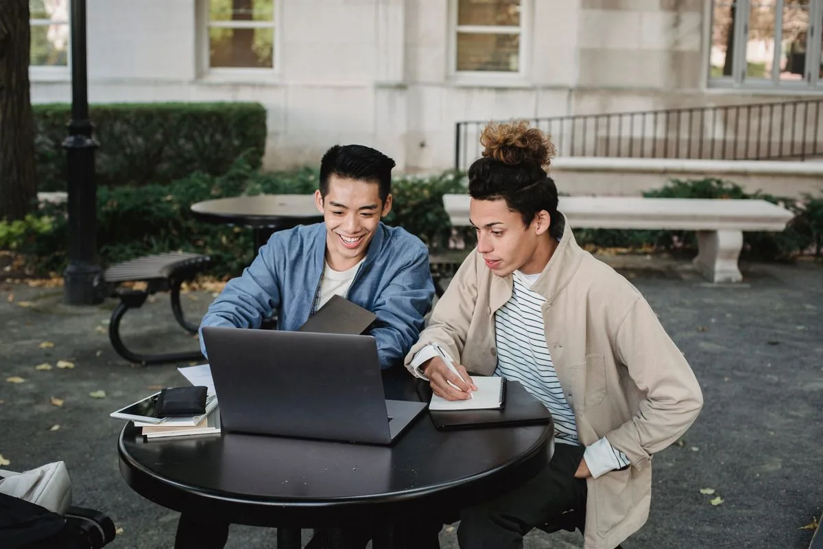 Two students working on a laptop outdoors on campus